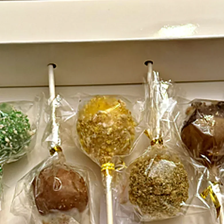 Individually Wrapped Cake Pops Close up of cake pops sealed in clear bags with gold ties, resting in a box with holes cut for the sticks
